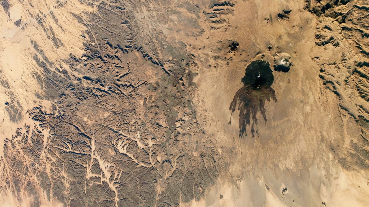 Shadowy tendrils of ancient lava have scarred a dark volcano next to a ‘skull’ in the Sahara — Earth from space